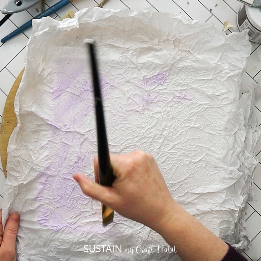 Painting crinkled tissue paper with purple paint.
