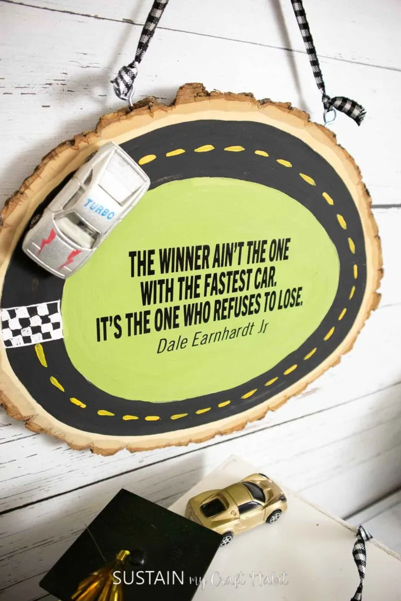 Wood slice painted as a race track with a quote and toy race car.