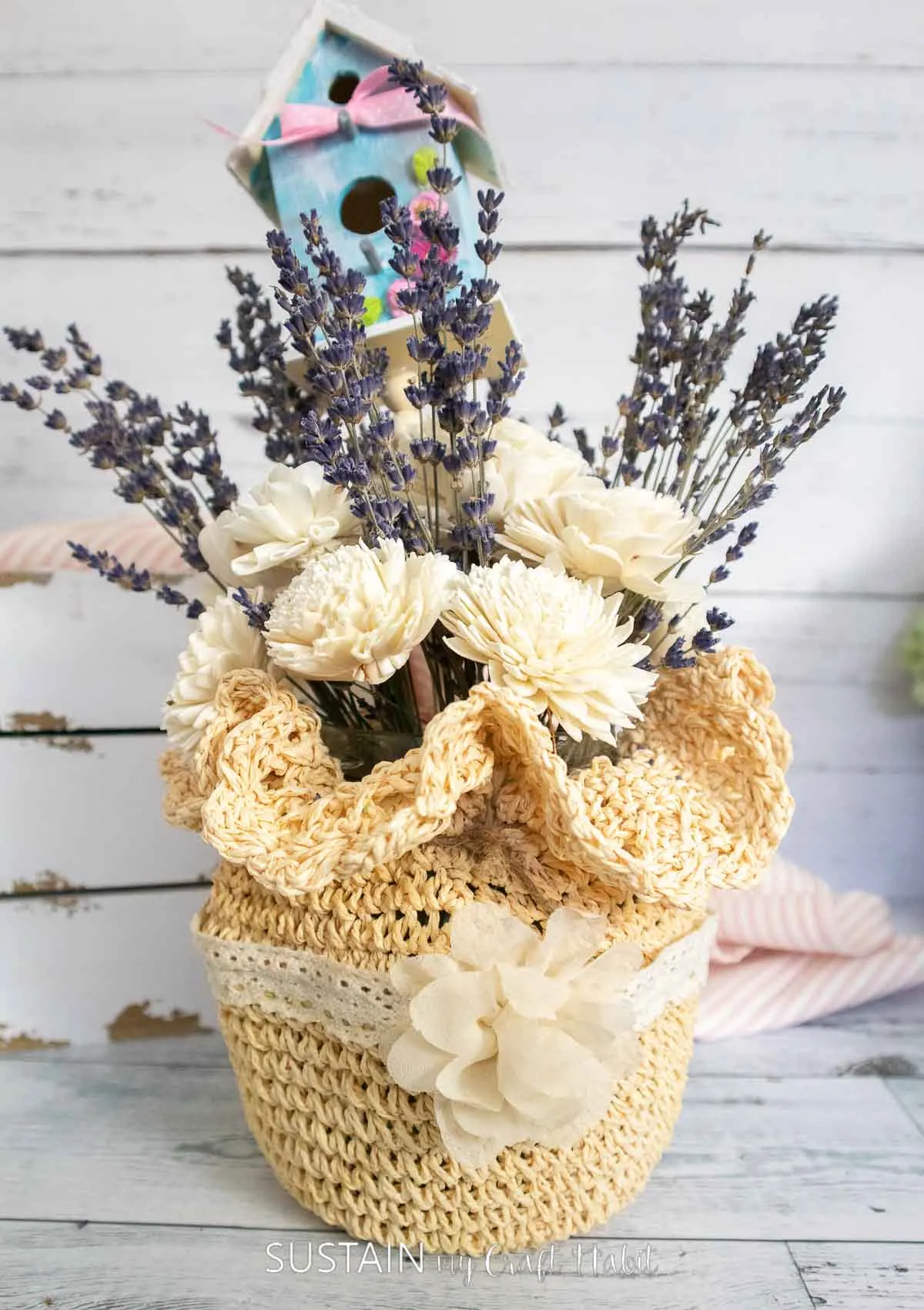 Birdhouse in lavender and flower in upside down straw hat brought together with twine. 