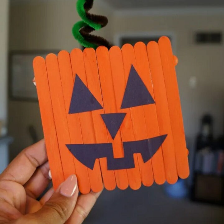 Hand holding a popsicle stick pumpkin.