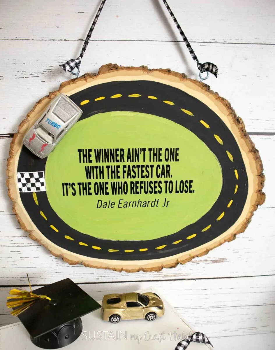 Wood slice painted as a race track with a quote and toy race car.