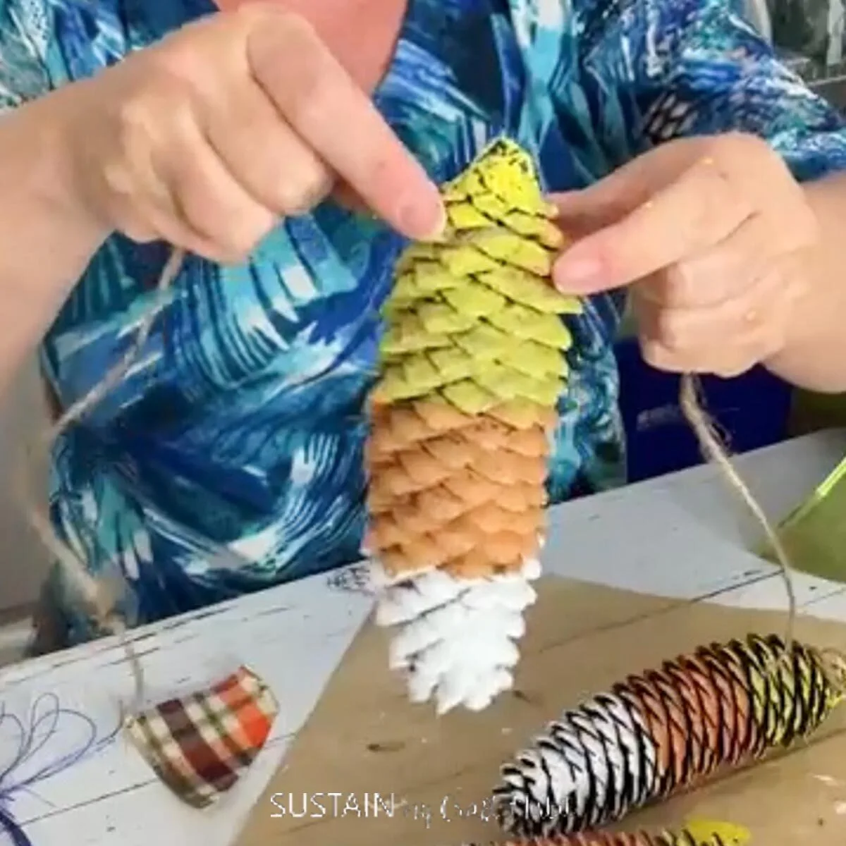 Attaching twine to a painted candy corn pine cone.