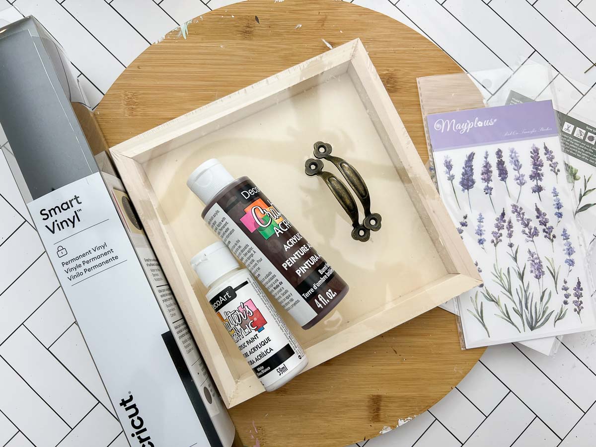 Materials needed to make trinket trays including a wood panel, paint and vinyl transfers.