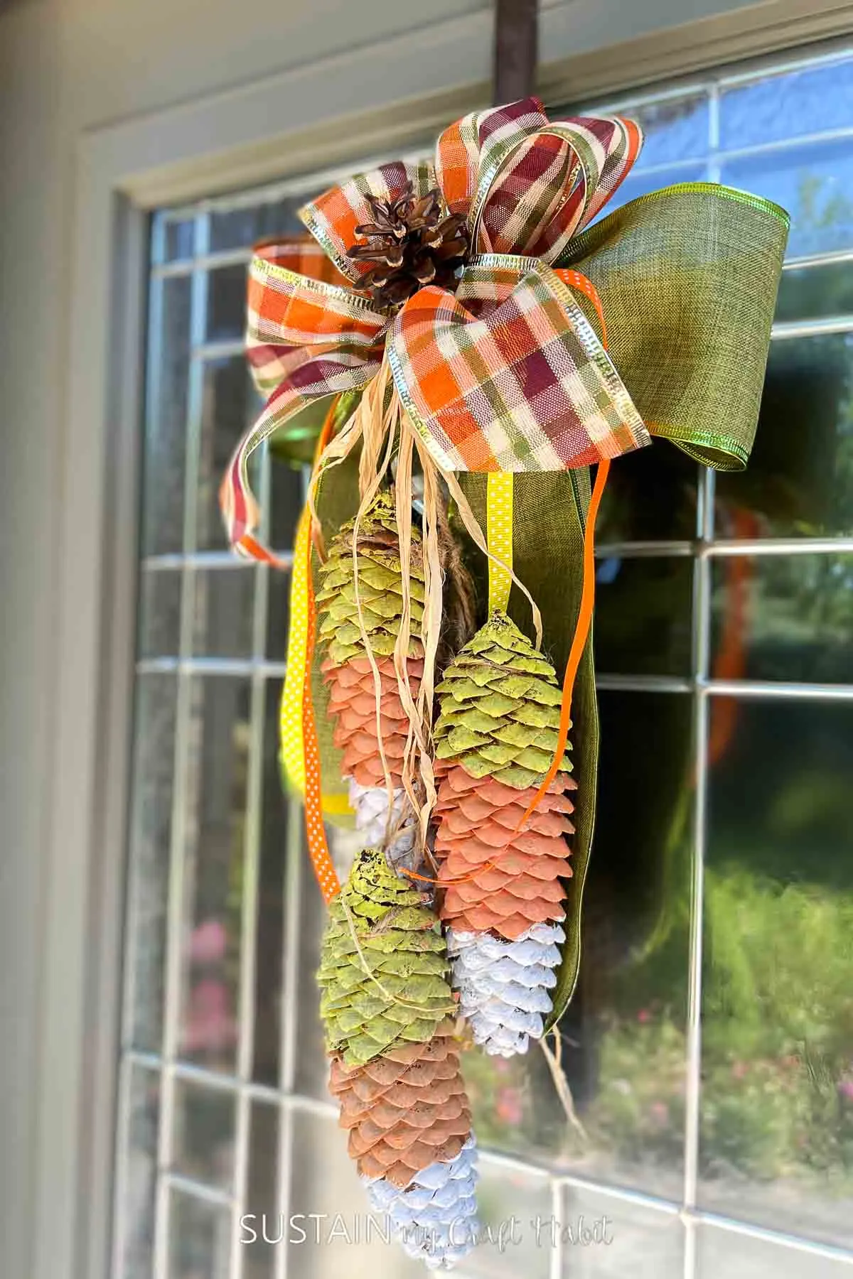 Candy corn decor made from painted pine cones and ribbon  hanging on a door.