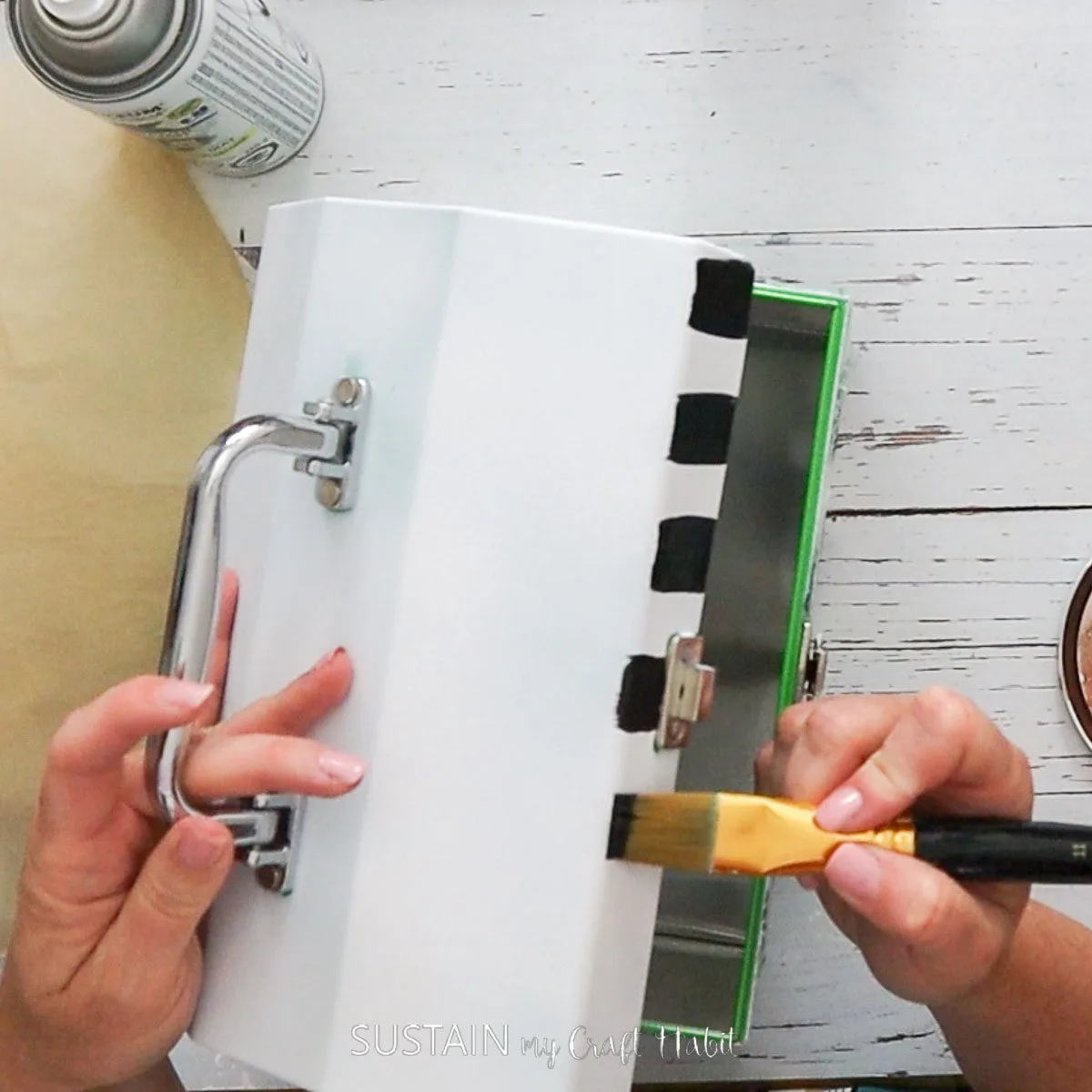 Painting black stripes onto a metal lunch box.