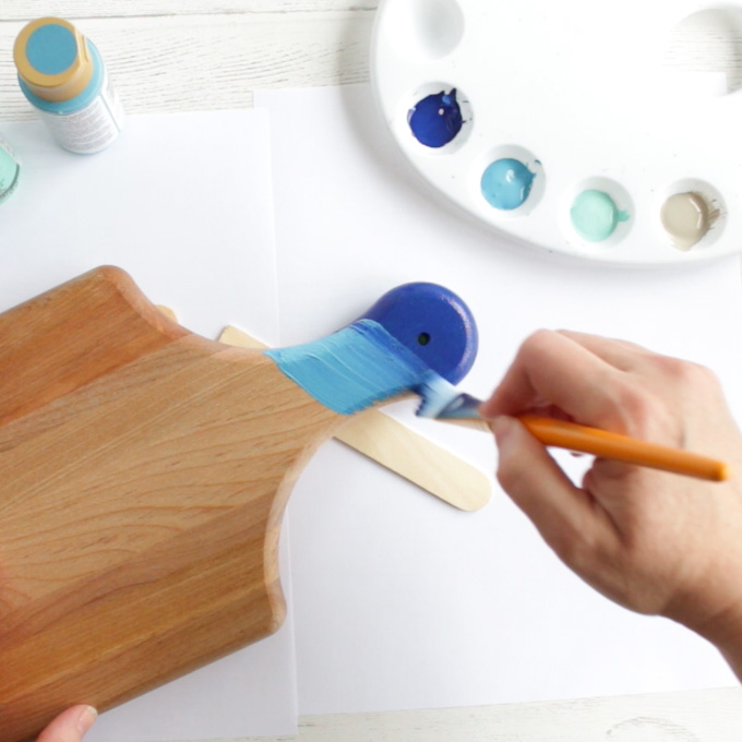 Painting a lighter blue colour onto a cutting board handle.
