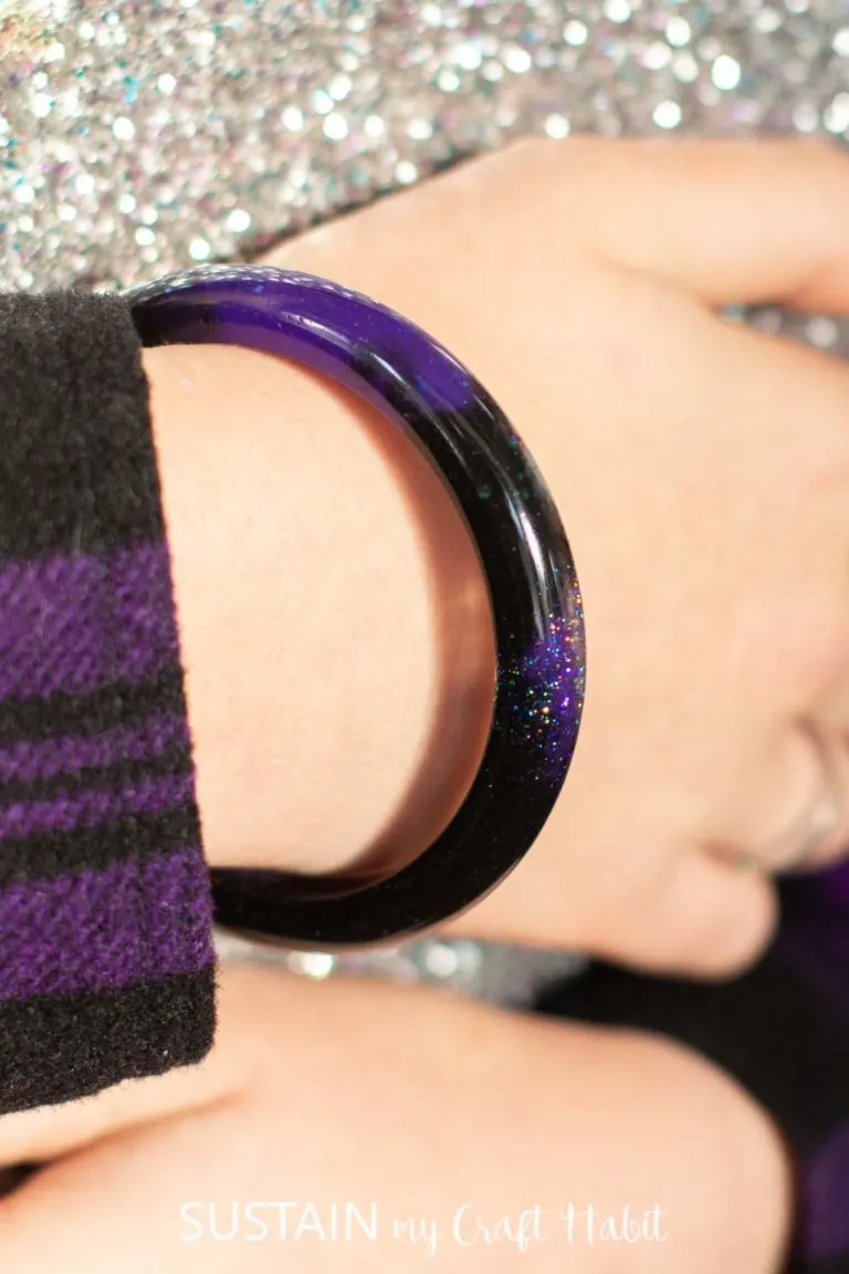 A dark black and purple resin bangle bracelet on the wrist of a young girl.
