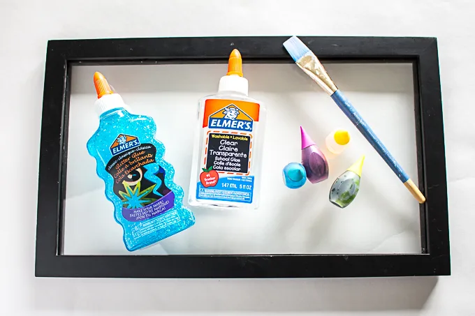 Materials needed to make an easy DIY faux stained glass art including picture frame, glue, paint brush and food coloring.