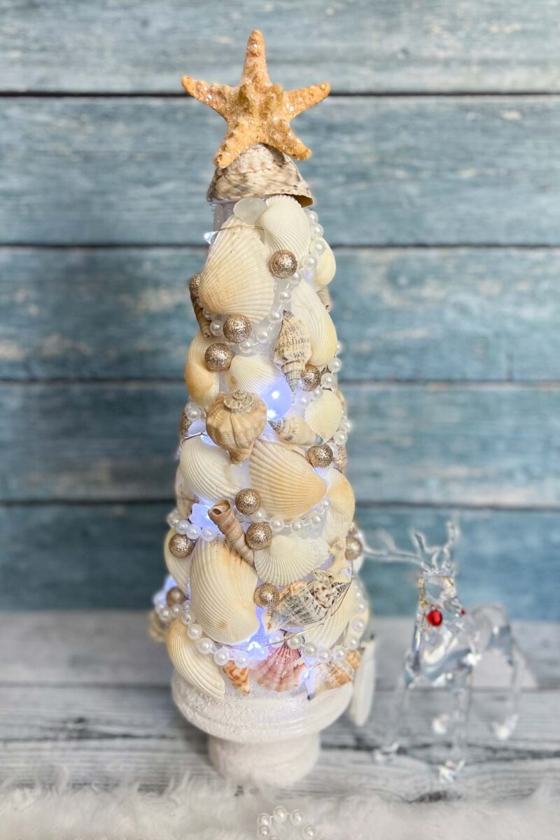 Tabletop Christmas tree decorated and seashells, pearls, twinkle lights and glitter.