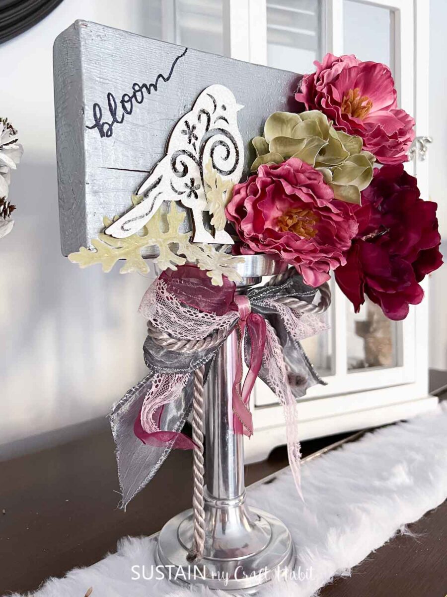 Faux floral wedding table centerpiece made with a candlestick, faux flowers, ribbon and embellishments.