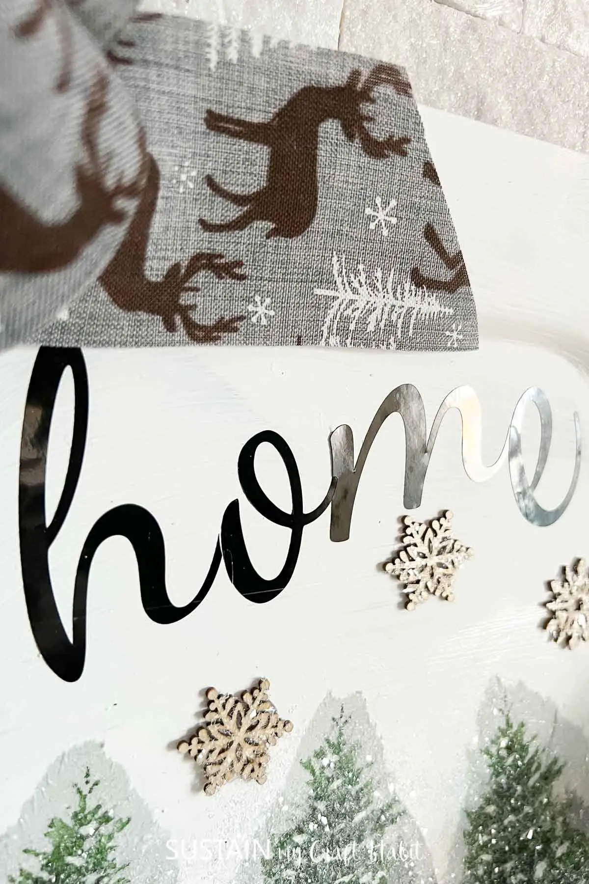 Close up of upcycled home sign made from a platter and decorated with ribbon, snowflakes, napkins and glitter.