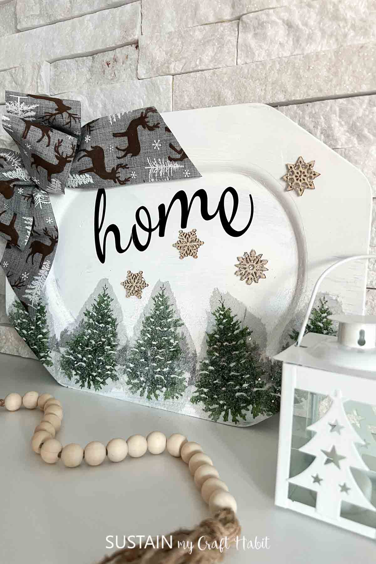 Upcycled home sign made from a platter and decorated with ribbon, snowflakes, napkins and glitter.