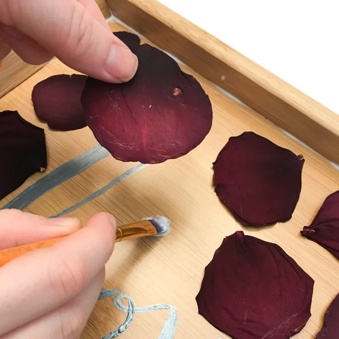 Gluing rose petals onto a wooden tray. 