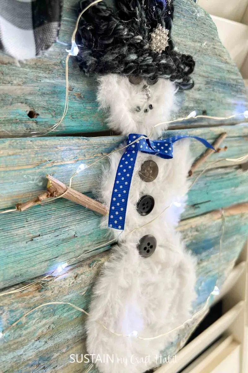 Close up of the wintry snowman craft on a painted driftwood sign.