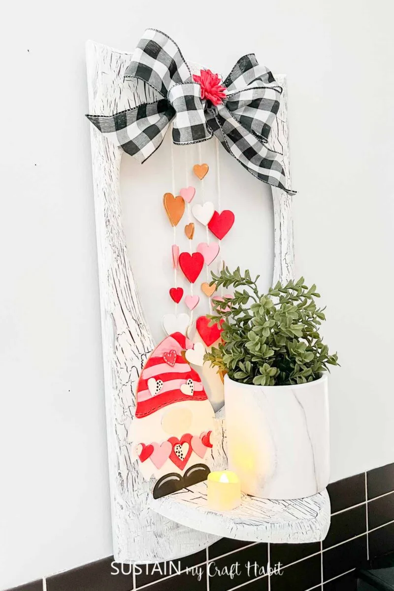 Upcycled wood shelf decorated for Valentine's Day with paint, ribbon, wood heart cut outs, a wooden gnome and a plant.