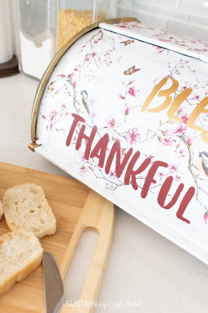 Close up of an upcycled bread box decorated with decoupage and the words "blessed" and "thankful."