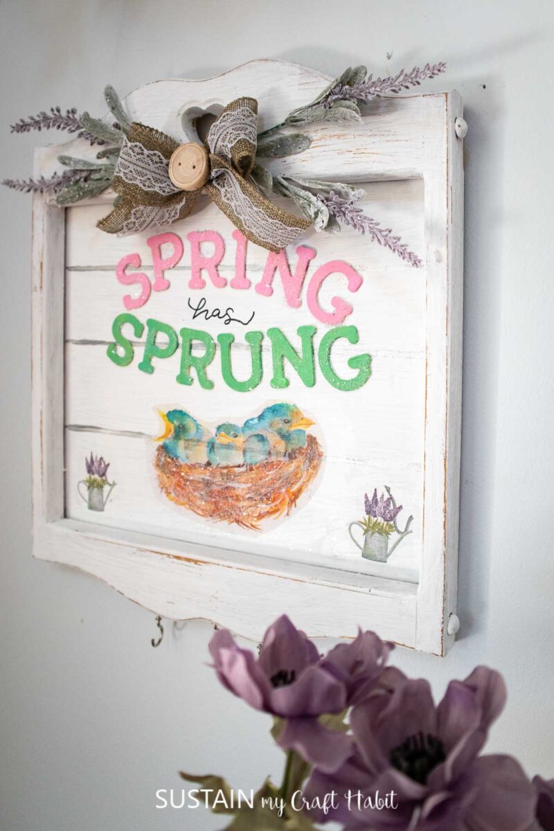Spring sign hung on a wall and decorated with birds, wooden letters, ribbon and flowers.