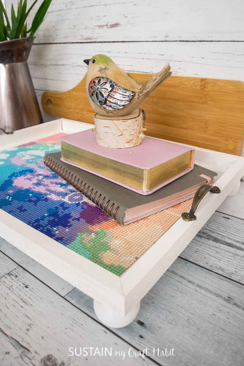 Sealed diamond art painting in a wood canvas tray stacked with books and decorative bird.