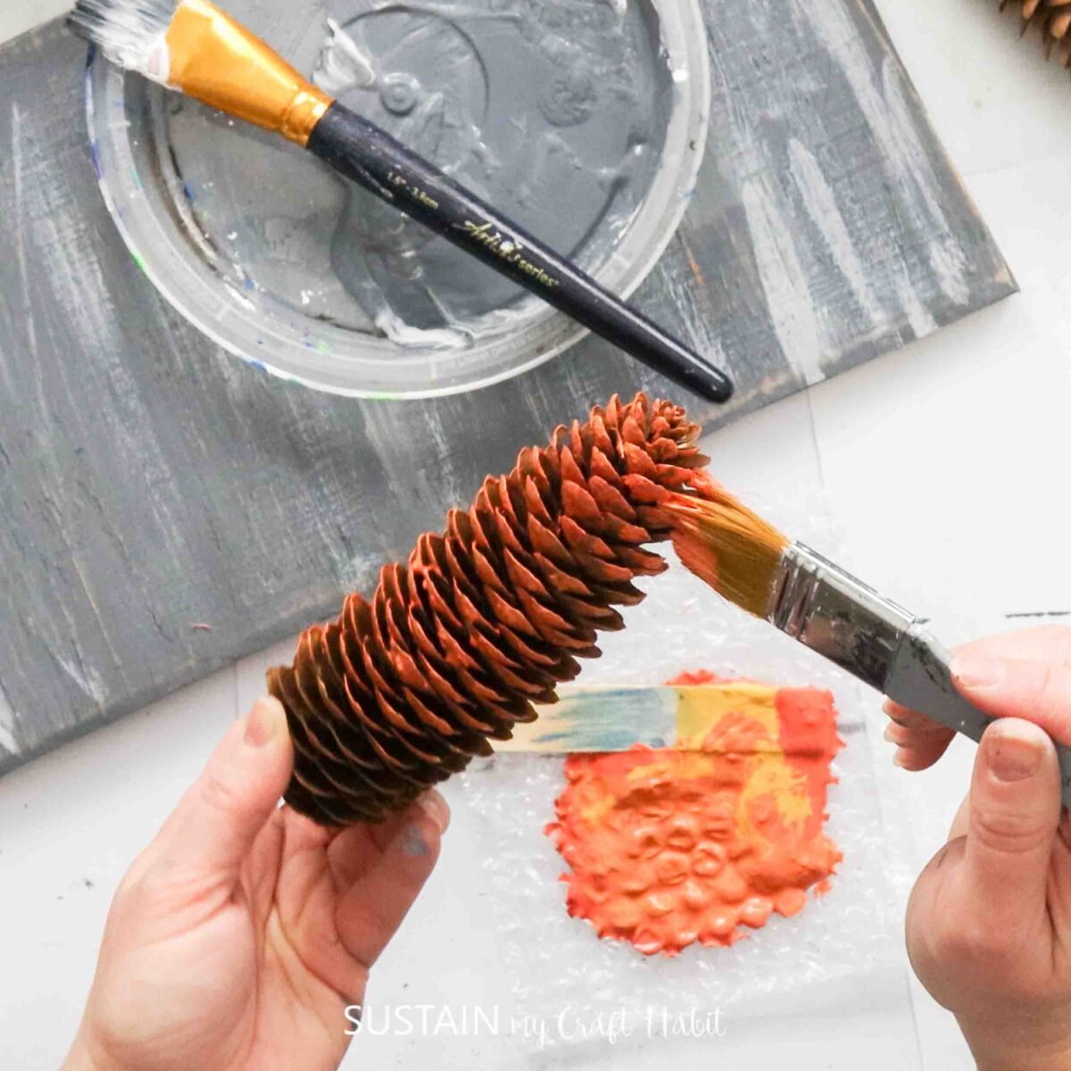 Painting a pinecone with orange paint.