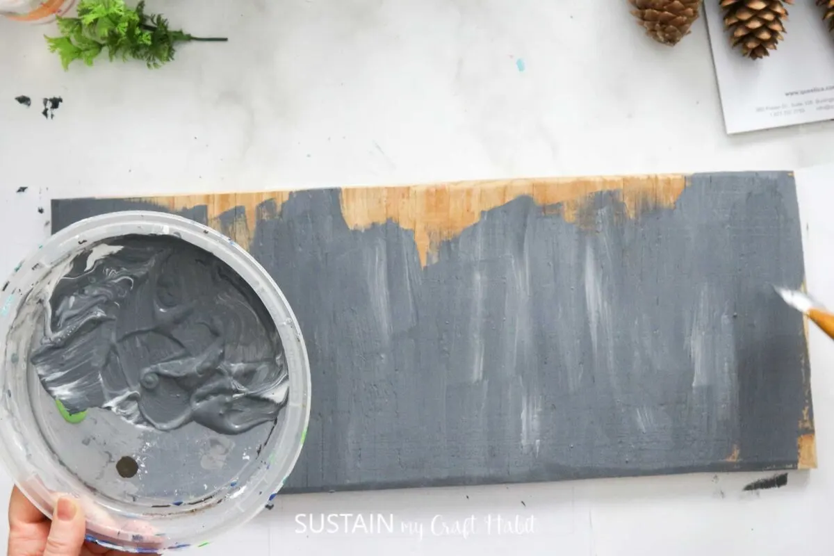 Painting a wood board with grey paint.