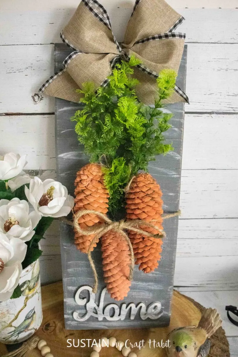 Pinecone carrot sign decorated with ribbon, twine, greenery and pinecones.