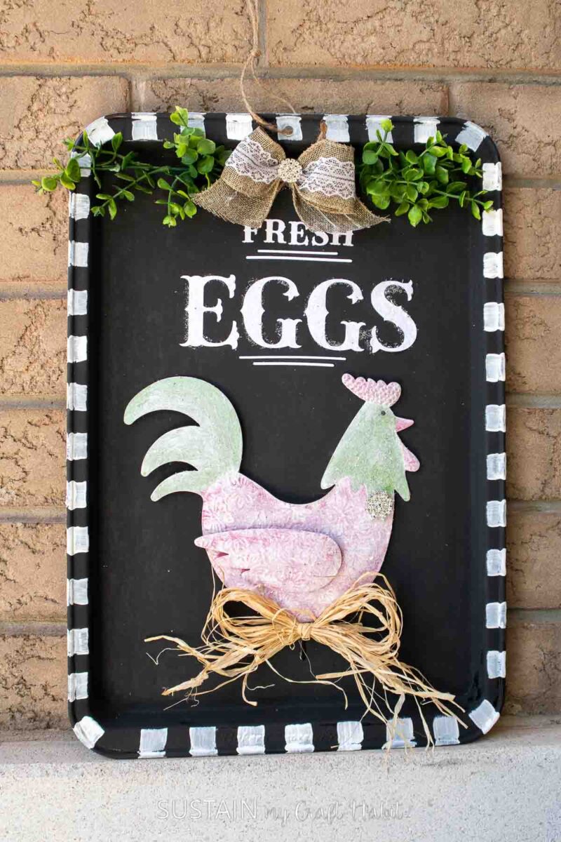 Upcycled cookie sheet turned into a farmhouse sign with decorative chicken, bows, and greenery.