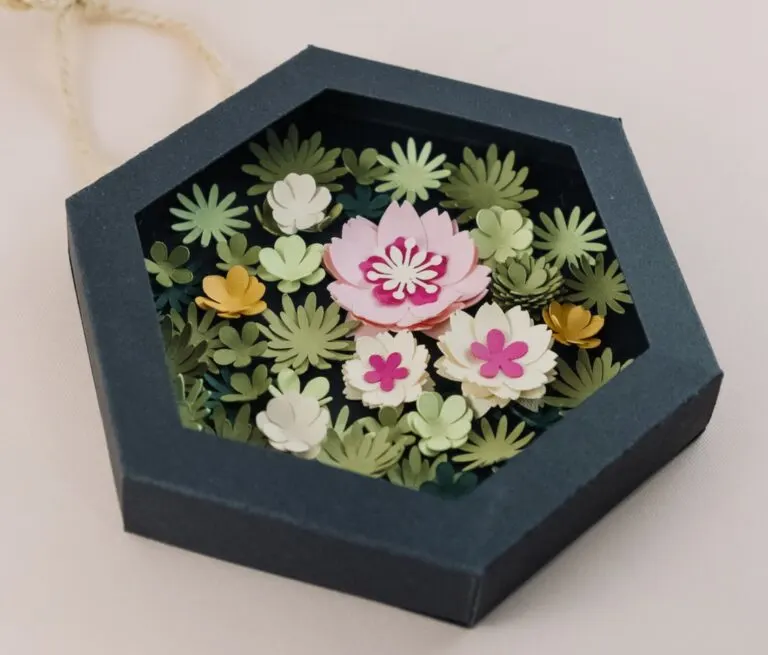 A dark gray hexagonal paper box filled with a variety of delicate paper flowers.