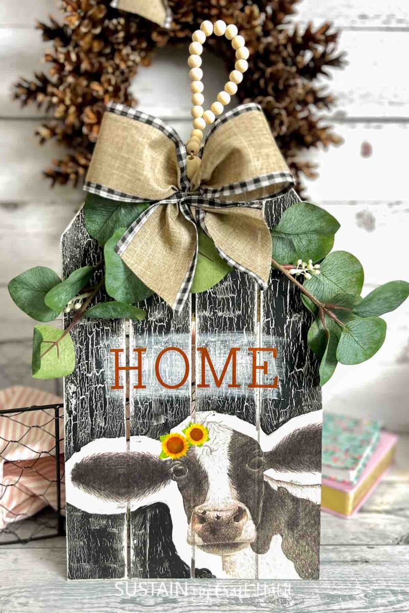 Farmhouse kitchen cow sign decorated with ribbon and greenery.