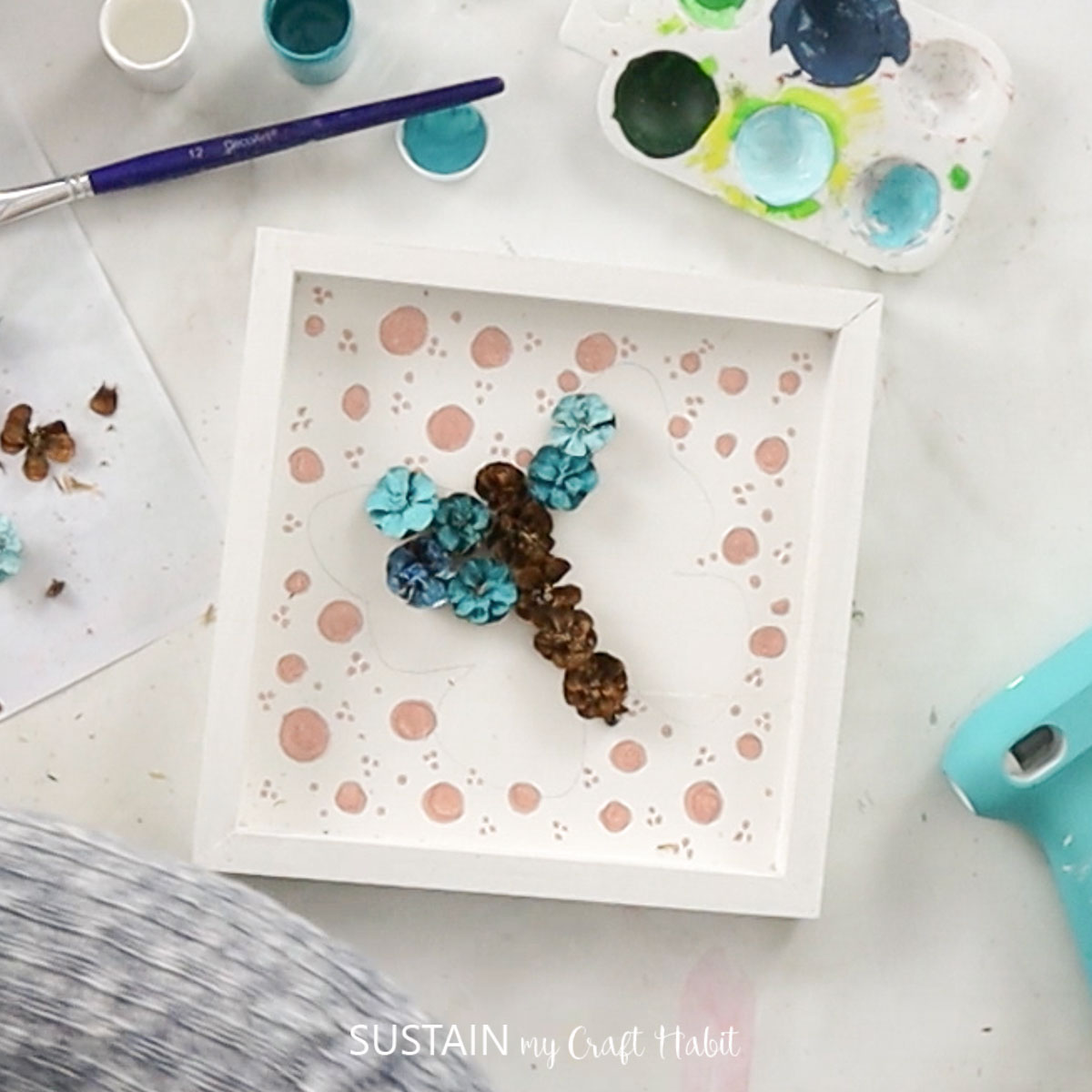 Gluing pinecones to the wood canvas.