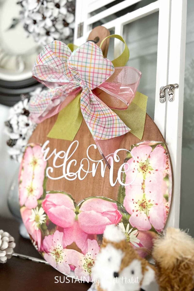 Wood board welcome sign decorated with napkins, ribbons and a vinyl phrase.
