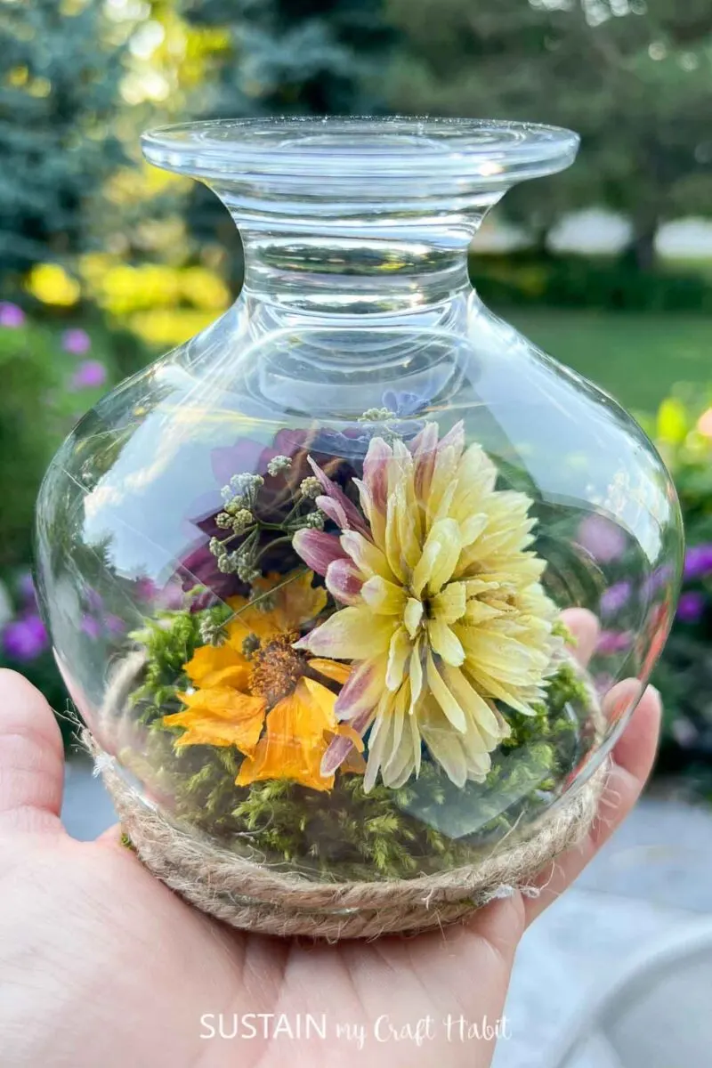 Hand holding a wine glass terrarium with dried flowers