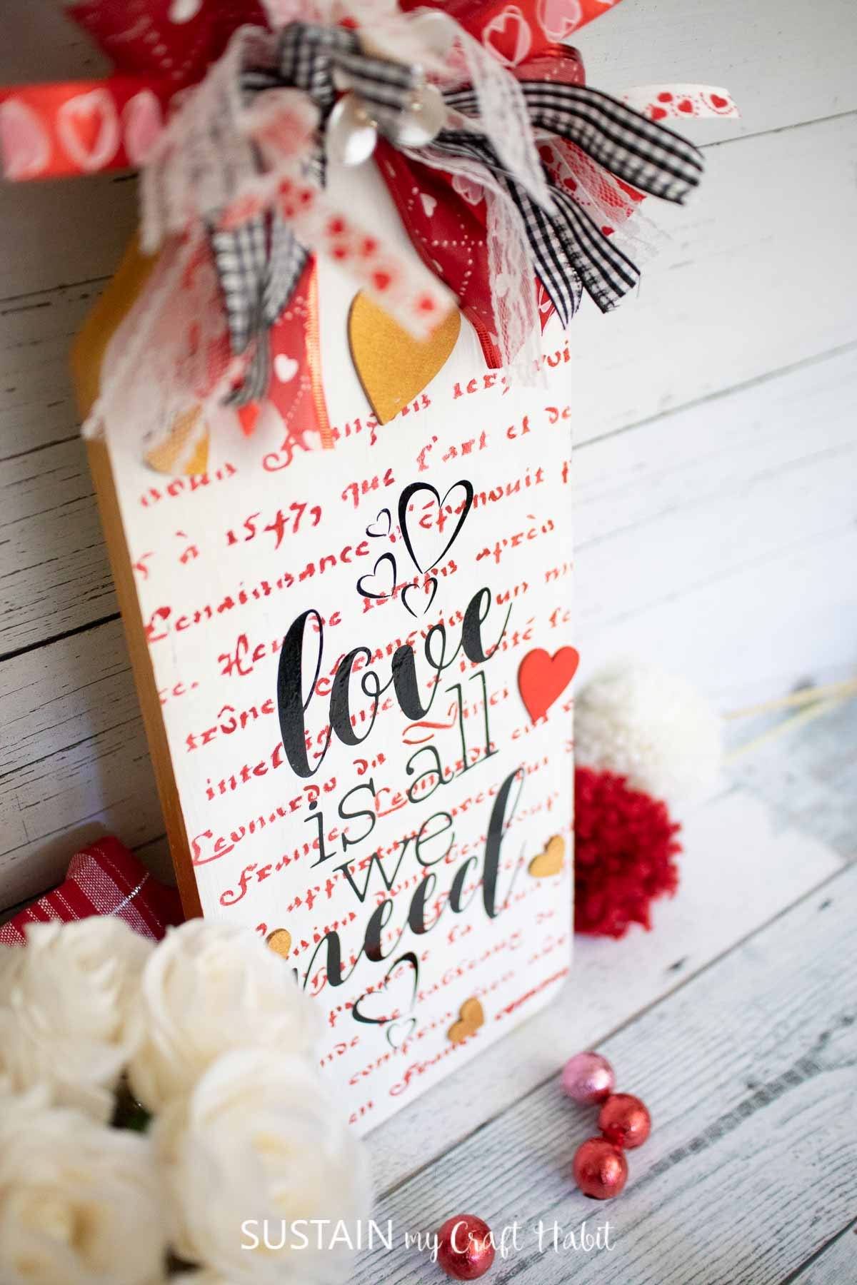 Wood panel Valentine's day sign painted and decorated with script, ribbon and a vinyl cutout.