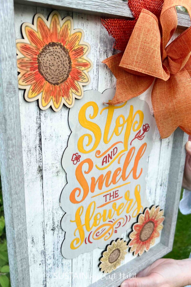 Fall sign decorated with sunflowers, a phrase and an orange bow.