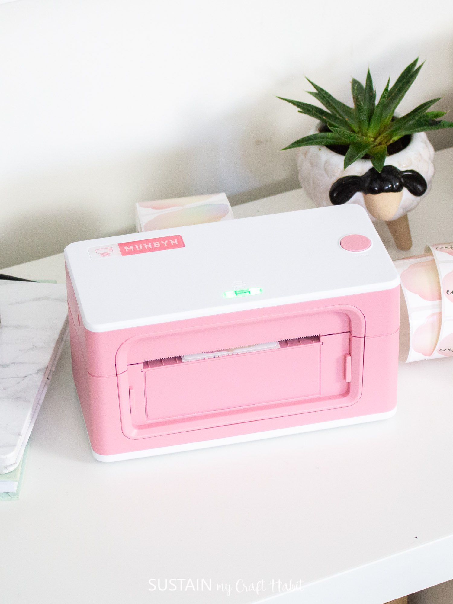 Pink Munbyn Thermal Label printer on a white surface surrounded by colorful stickers and a small plant.