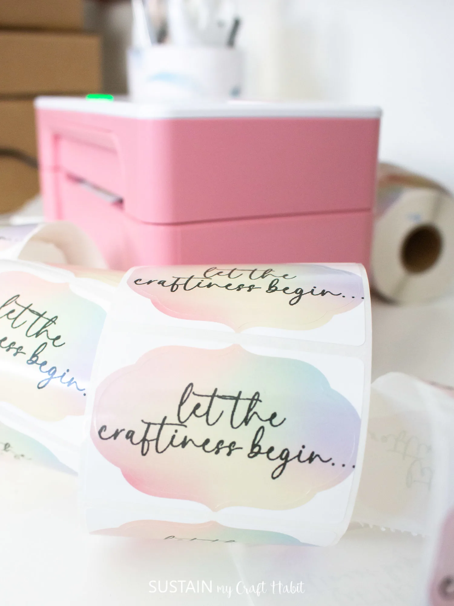 Close up image of rainbow colored sticker printed with the phrase "let the craftiness begin...".
