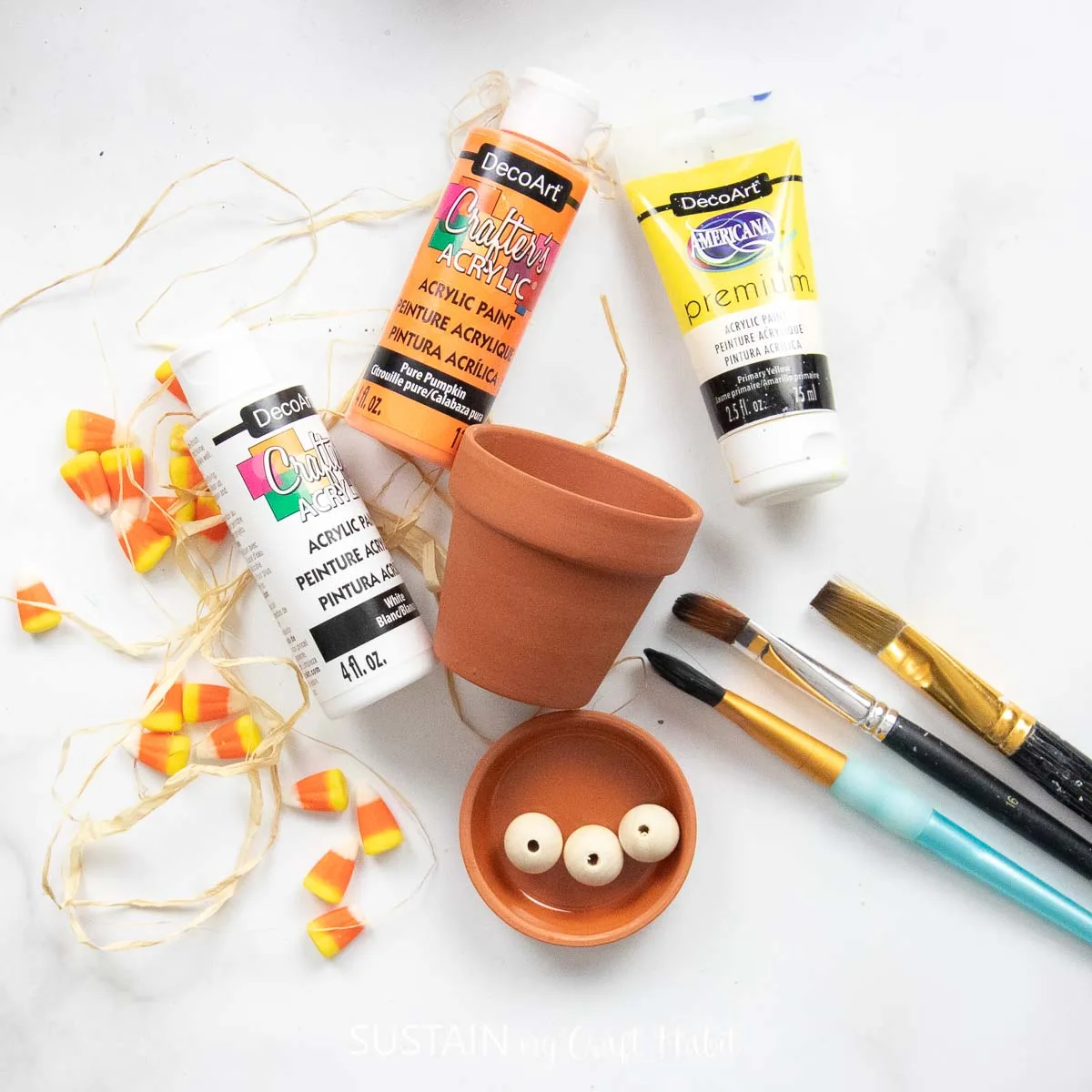 Materials needed to make a candy corn craft with clay pots, paint, paintbrushes and ribbon.