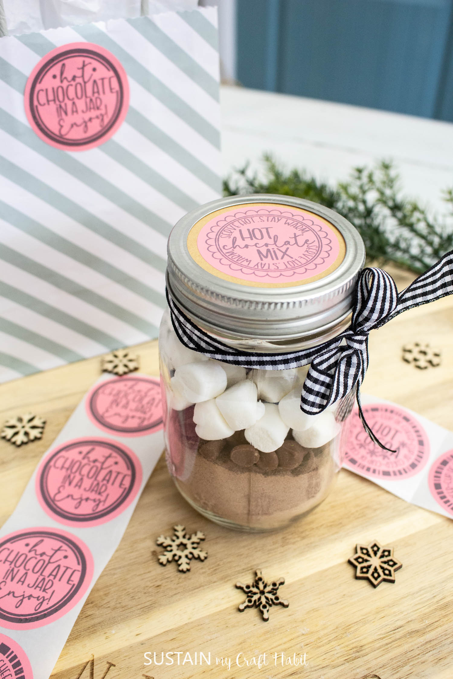 Mason jar filled with hot chocolate, chocolate chips and marshmellows. A cute pink hot chocolate label is on top of the lid and a pretty ribbon is wrapped around the jar. 