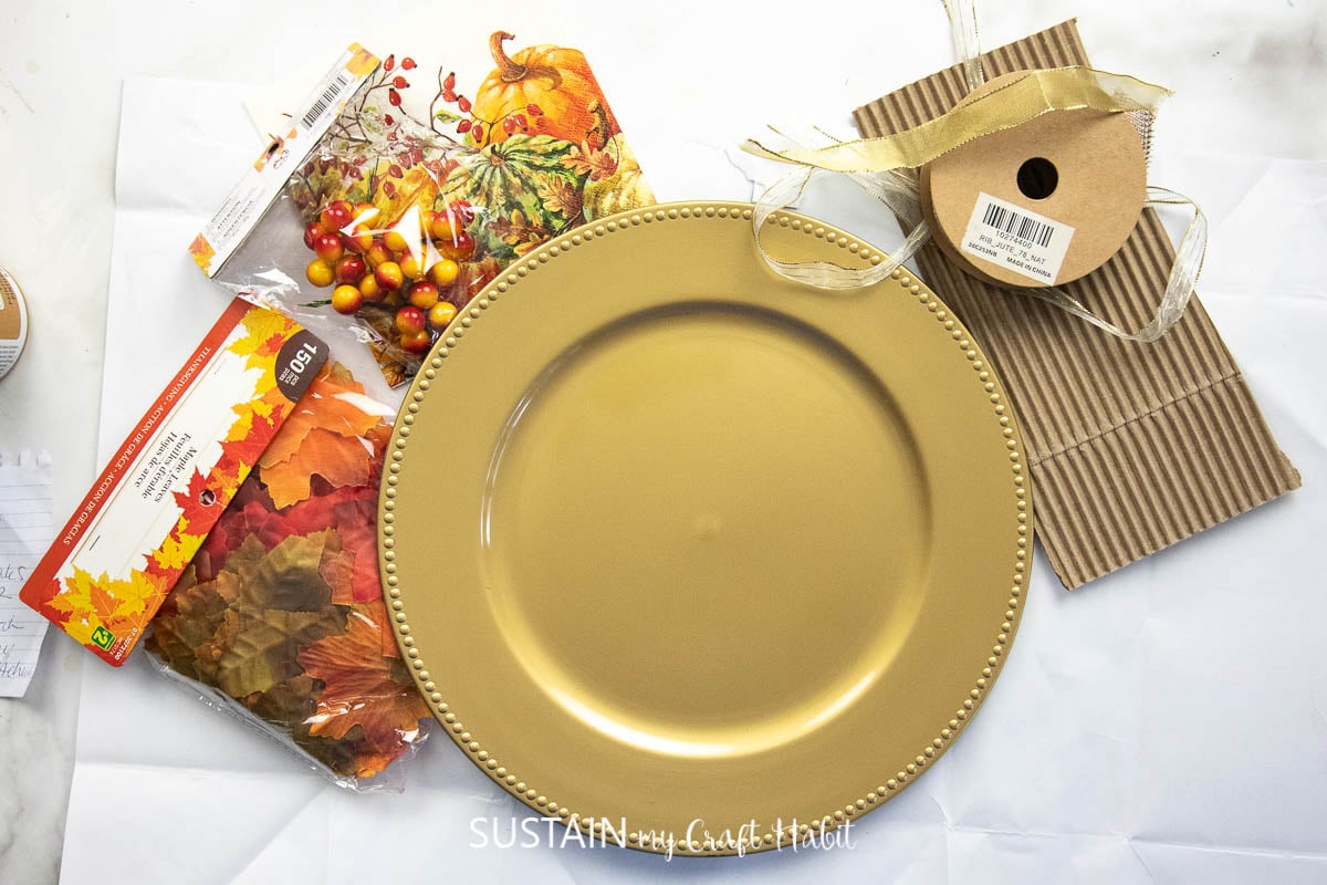 Materials needed to make a fall harvest dollar store charger craft including a gold charger, ribbon and embellishments.