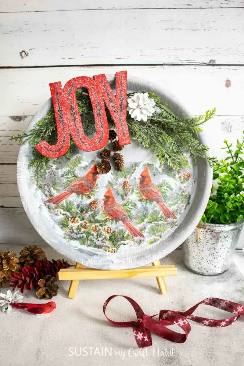 Wood tray decoupaged with cardinal paper napkins and embellished with a joy sign, greenery and pinecones.