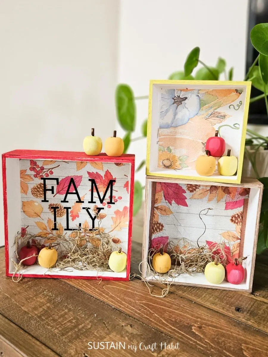 Fall themed trinket boxes stacked and decorated with napkins, moss and decorative apples.