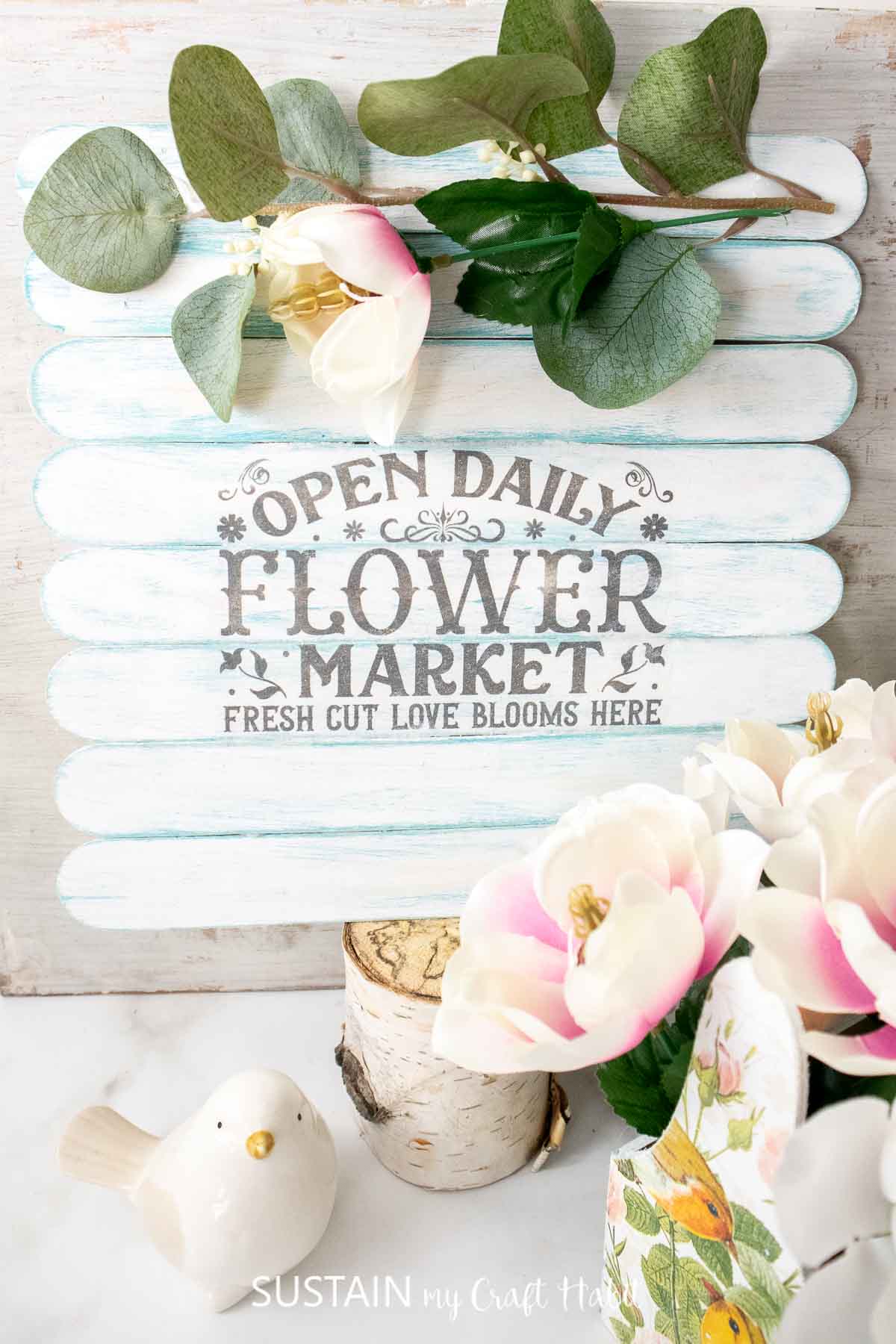 Jumbo craft stick sign decorated with a printed image and faux flowers.