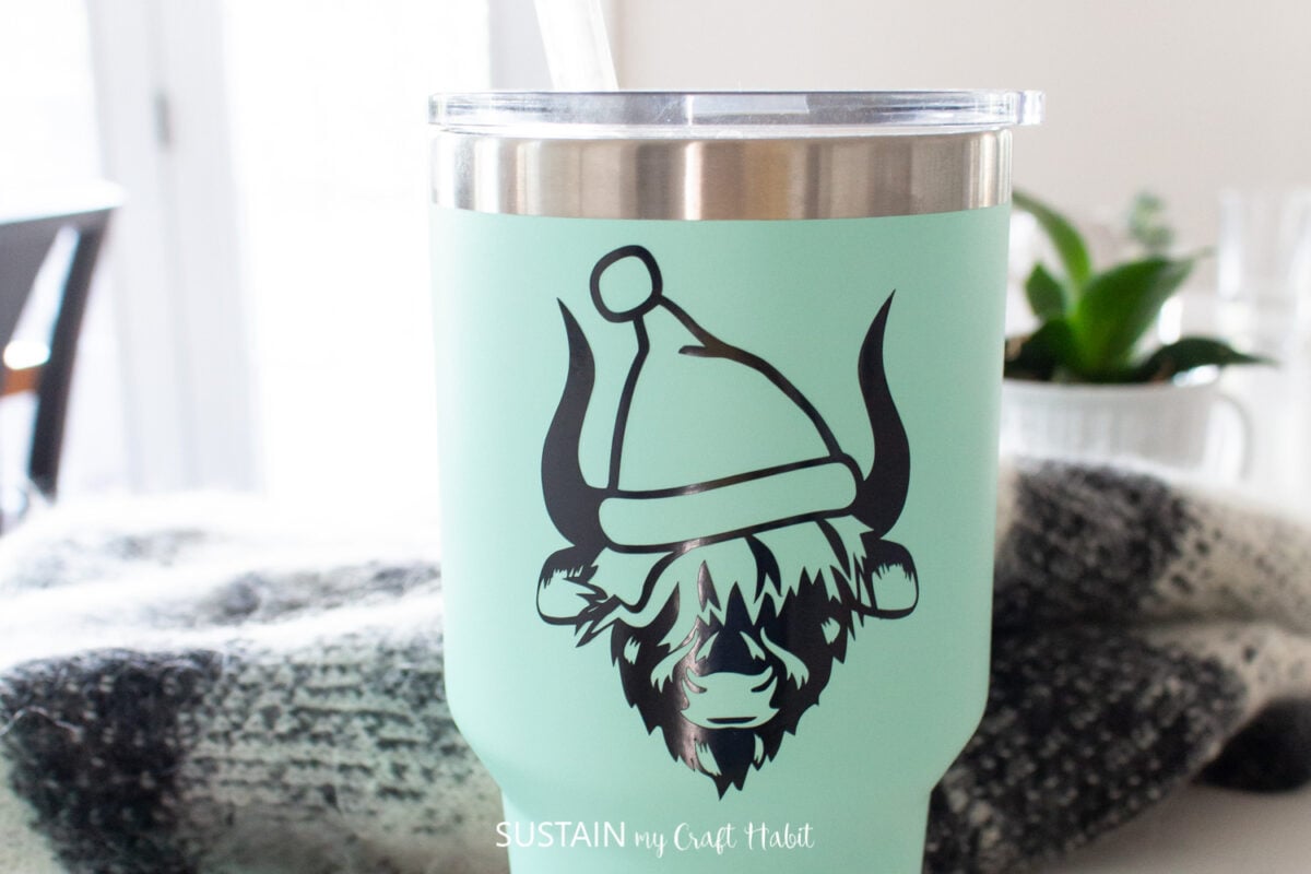 Teal tumbler decorated with a vinyl Highland cow wearing a Santa hat.