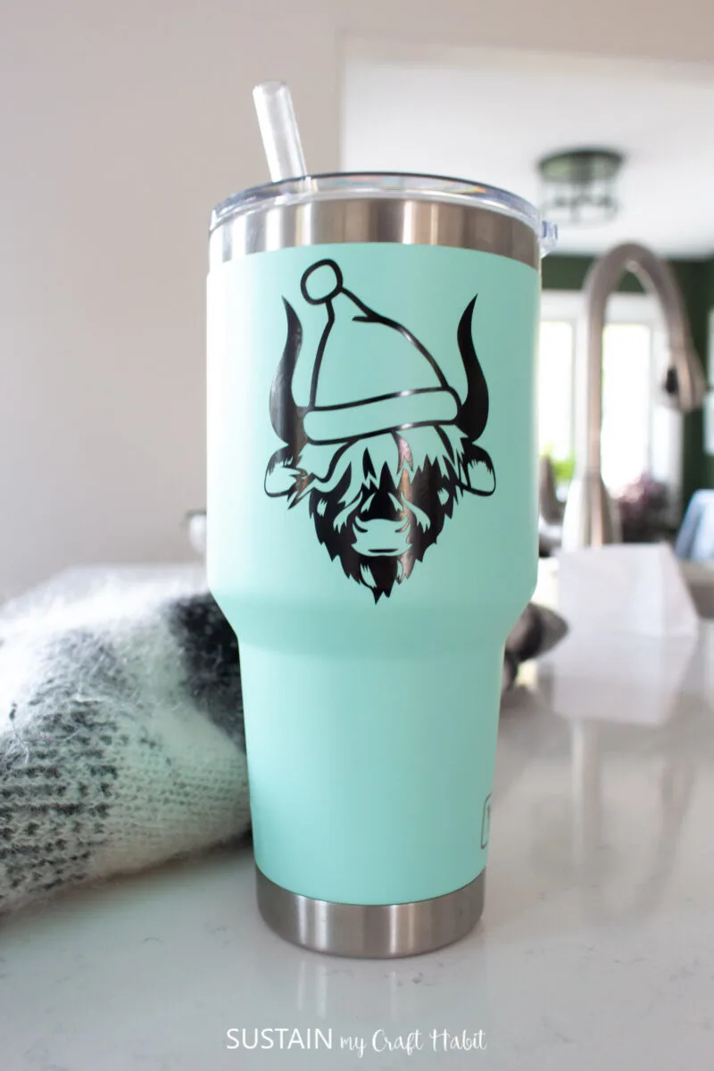 Teal tumbler decorated with a vinyl Highland cow wearing a Santa hat.
