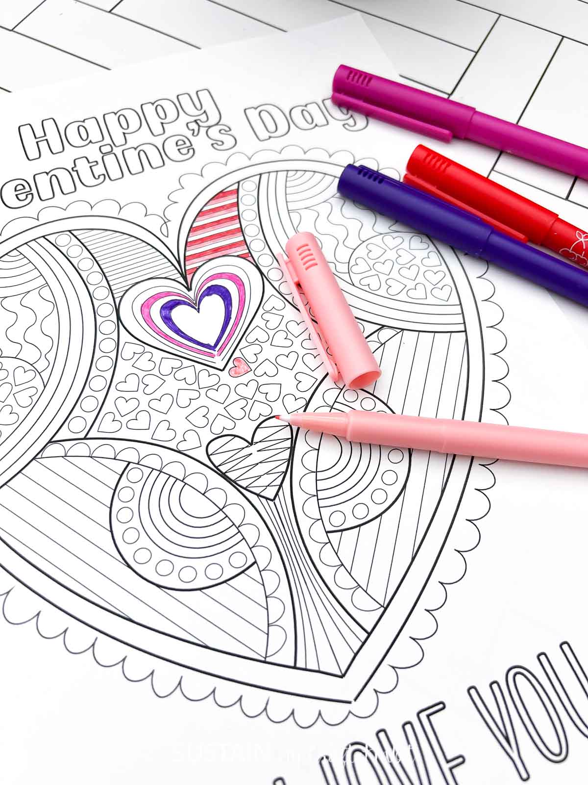 Open pink marker laying on a Valentine's day heart coloring page.