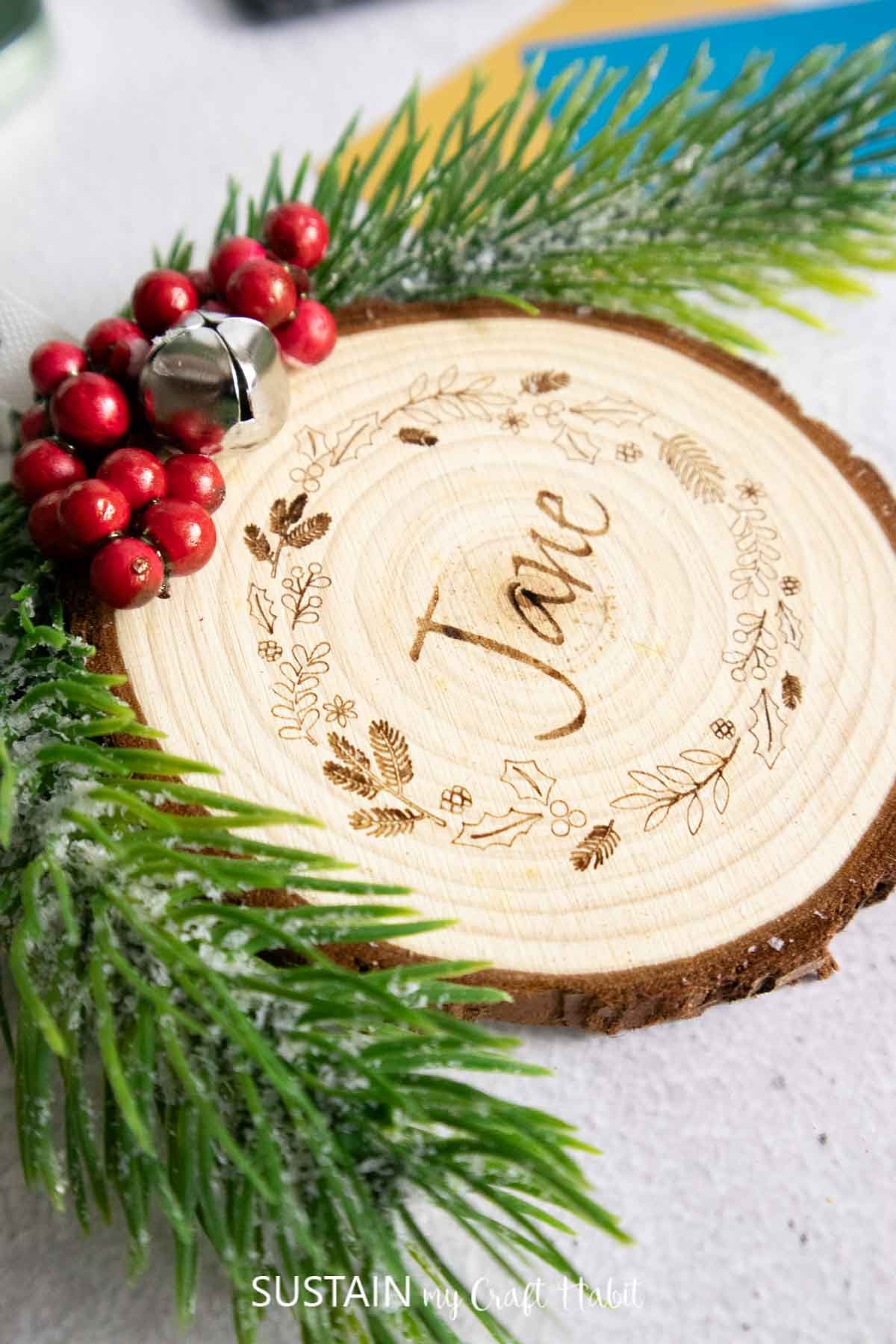 Close up of the surface of a wood slice engraved with a wreath motif and the name Jane.