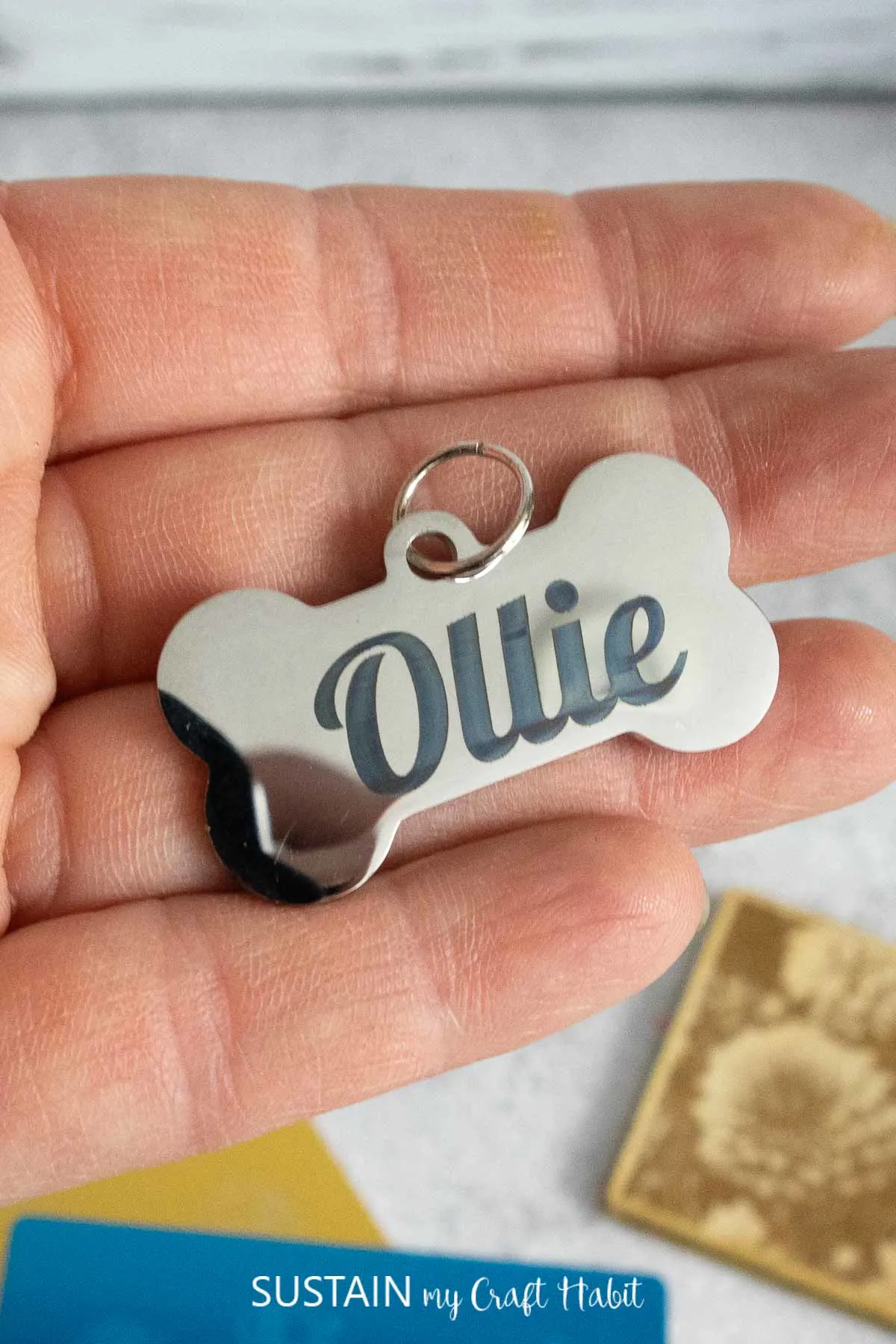 Close up image of a stainless steel bone-shaped pendant engraved with the name Ollie.