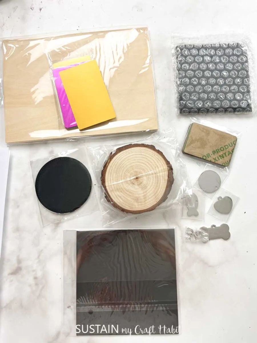 Materials included with the xTool F1 laser engraver including wood slices, black acrylics, slate coaster, plywood sheet, metal tags, faux leather coasters and photo paper.