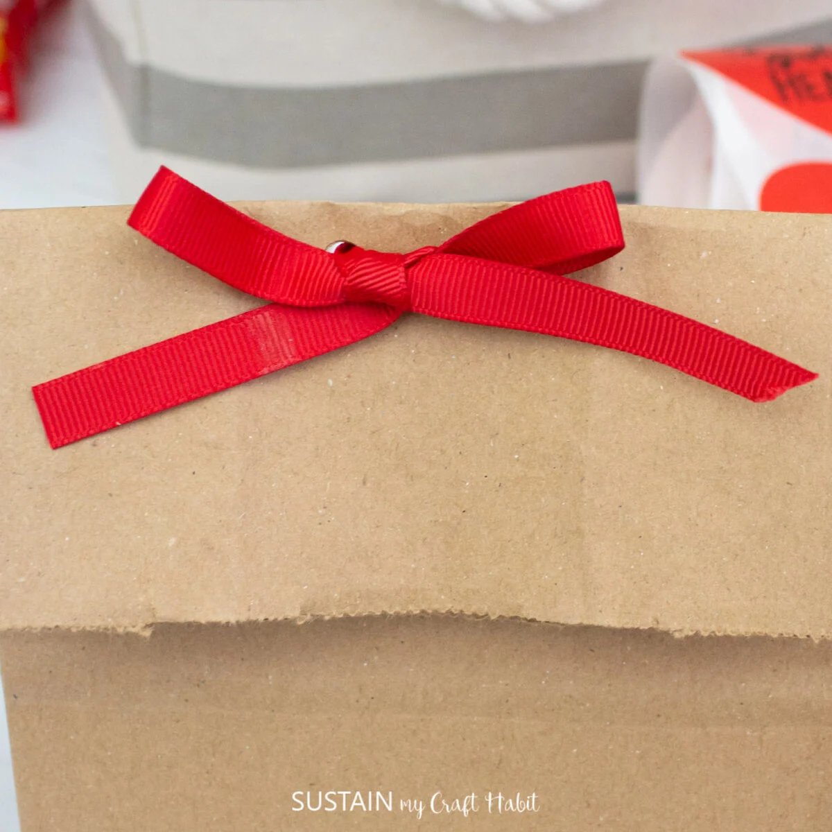 Attaching a red ribbon to the top of a paper bag.
