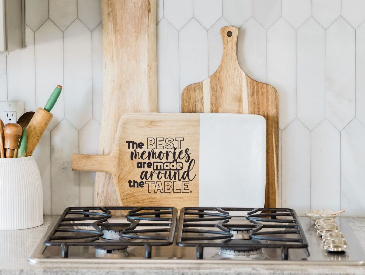 Laser engraved cutting board leaned up against a kitchen wall with other cutting boards.