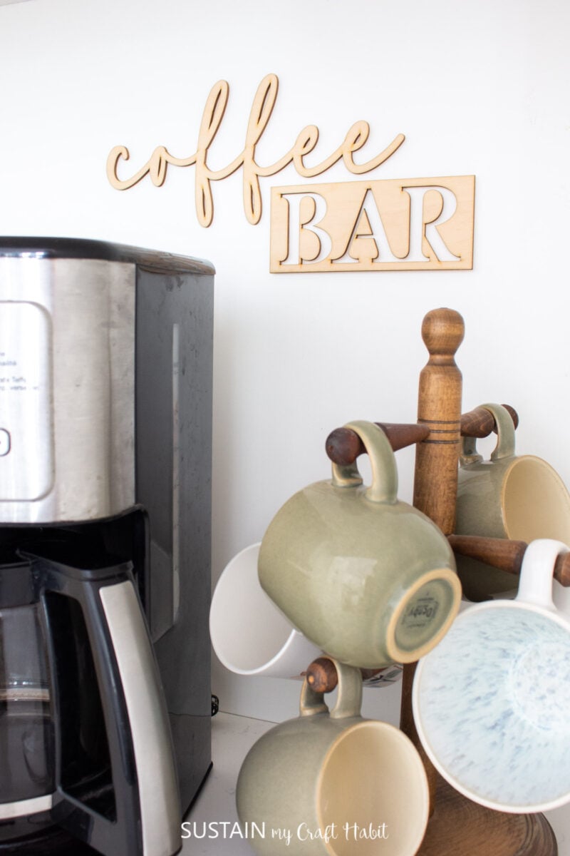 Coffee bar sign on a wall next to a coffee maker and mugs.